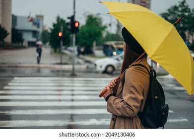 Young beautiful woman standing on a crossroad and holding a yellow umbrella in the city during rain - Powered by Shutterstock