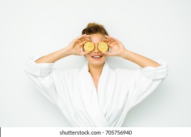 Young Beautiful Woman Standing On A White Wall In Bath Towel Playing With Her Favorite Fruit, The Lemon