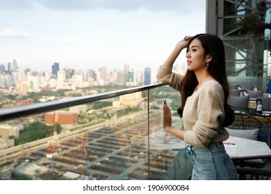Young beautiful woman standing outside the building on rooftop floor restaurant to see the city view in the evening, feeling happy and relaxation with city skyline