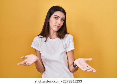 Young beautiful woman standing over yellow background clueless and confused with open arms, no idea concept. 
