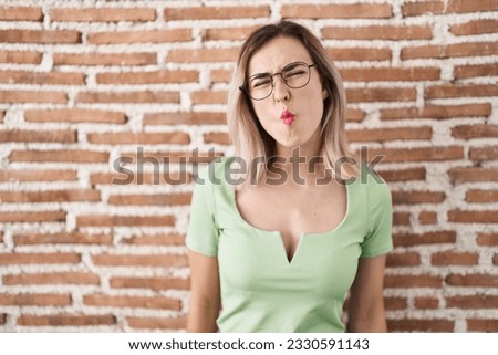 Young beautiful woman standing over bricks wall making fish face with lips, crazy and comical gesture. funny expression. 