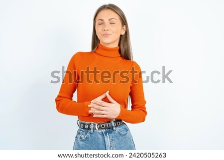 Young beautiful woman standing over white studio background touches tummy, smiles gently, eating and satisfaction concept.