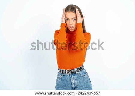 Young beautiful woman standing over white studio background with scared expression, keeps hands on head, jaw dropped, has terrific expression. Omg concept