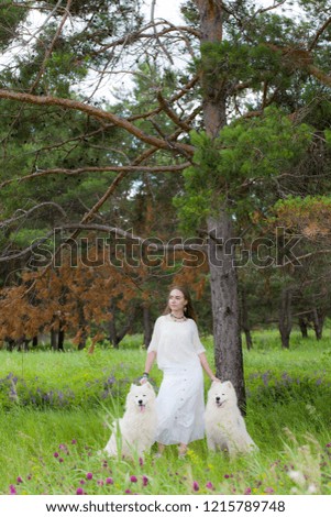 young beautiful woman standing with two big white shaggy dogs on a background of forest in the green grass