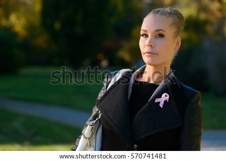 Young beautiful woman standing while wearing pink ribbon for symbol of breast cancer awareness