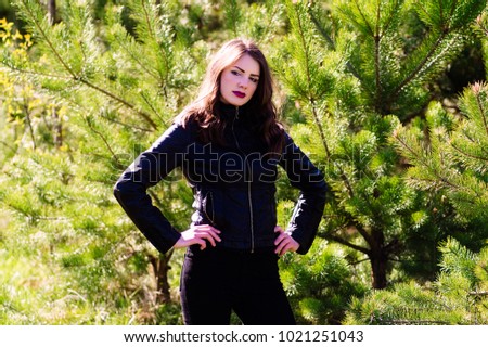 Young beautiful woman in the summer in the woods among the trees. Black pants and a jacket