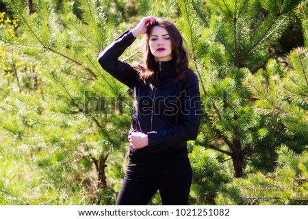 Young beautiful woman in the summer in the woods among the trees. Black pants and a jacket . Hand around the head.