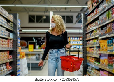 Young Beautiful Woman In A Supermarket Wearing Protective Face Mask And Holding Shopping Basket While Grocery Shopping