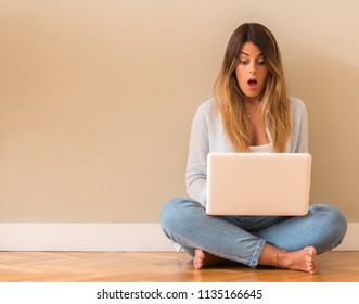 Young Beautiful Woman Suprised Sitting On The Floor With Computer Looking At The Laptop.