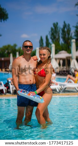 Young beautiful woman in a swimsuit and athletic man in glasses with inflatable ring in water park