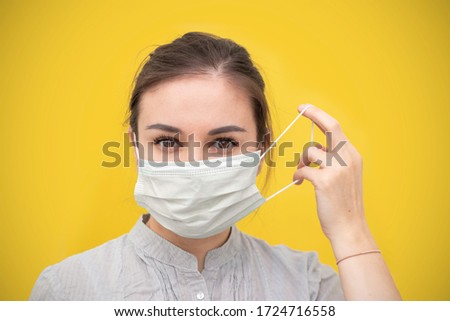 Young beautiful woman takes off protective sterile medical mask on a yellow background. Happy end. Victory over coronavirus. Pandemic Covid-19.