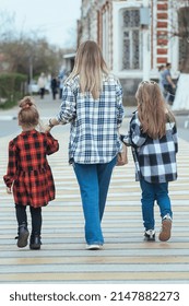 young beautiful woman takes two girls across the road in the city. Mom holds her daughters hands and teaches them to cross the road safely at a pedestrian crossing