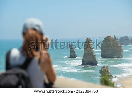 Young beautiful woman taking photos at Twelve Apostles rock formations at the great ocean road in sunny weather with a blue sky, Victoria, Australia, focused on the background, woman is blurred
