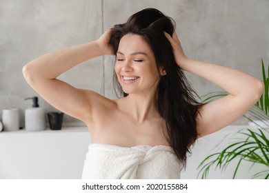 Young Beautiful Woman Touching Her Wet Hair To Dry It. Caucasian Girl With Brown Hair Making Volume Wearing Spa Bath Towel At Home After Taking A Shower.