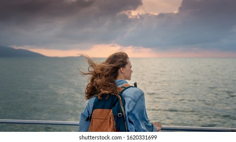 Young beautiful woman traveler with a backpack on the ship admiring the landscape at sunset. Travel Freedom Vacation concept