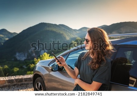 Young beautiful woman traveling by car in the mountains using smartphone at sunset