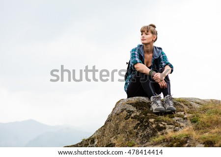 young beautiful woman traveling on mountains with backpack on her back, resting on a rock and and watching the view