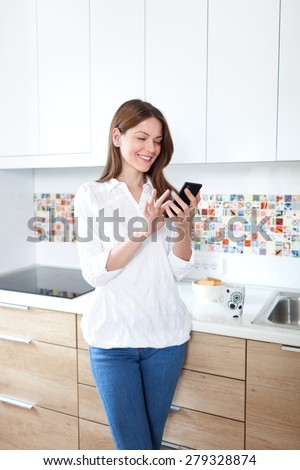 Young beautiful woman using cell phone and having fun in the kitchen