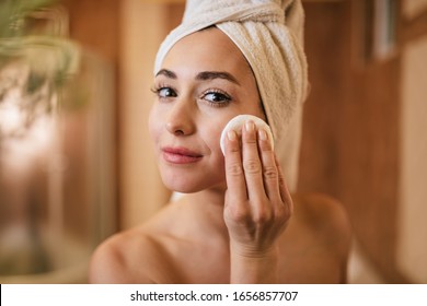 Young Beautiful Woman Using Cotton Pad While Cleaning Her Face In The Bathroom. 