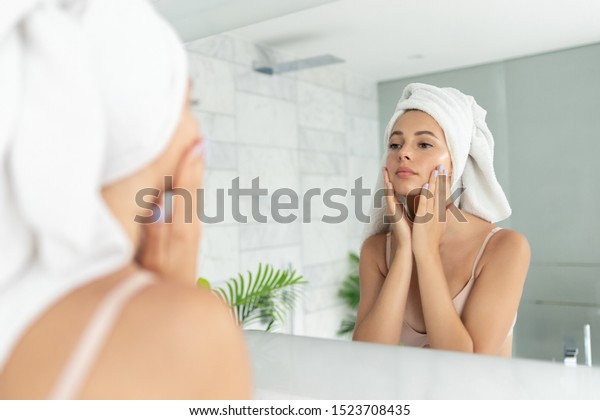 お風呂に入った後 スキンクリームの保湿ローションを使った若い美女 家庭用トイレの鏡の前に頭にタオルをかぶったかわいい女の子 毎日の衛生とスキンケア の写真素材 今すぐ編集