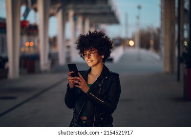 Young beautiful woman waiting on a train station platform and using smartphone in the night. Woman with afro hair using smartphone while standing on the railway station platform. - Powered by Shutterstock