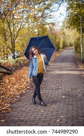 A Young Beautiful Woman Is Walking Along The Autumn Park With An Umberella In Her Hands. Autumn Portrait Of Young Happy Woman. Autumn. Rain.