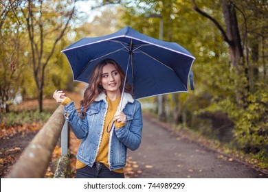 A Young Beautiful Woman Is Walking Along The Autumn Park With An Umberella In Her Hands. Autumn Portrait Of Young Happy Woman. Autumn. Rain.