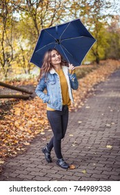 A Young Beautiful Woman Is Walking Along The Autumn Park With An Umberella In Her Hands. Autumn Portrait Of Young Happy Woman. Autumn. Rain.