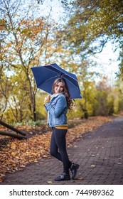 A Young Beautiful Woman Is Walking Along The Autumn Park With An Umberella In Her Hands. Autumn Portrait Of Young Happy Woman. Autumn. Rain.