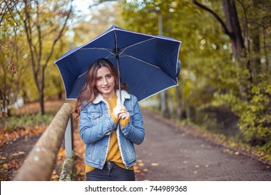 A Young Beautiful Woman Is Walking Along The Autumn Park With An Umberella In Her Hands. Autumn Portrait Of Young Happy Woman. Autumn. Rain.