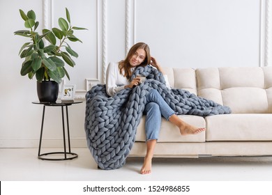 Young Beautiful Woman In Warm Chunky Knitted Blanket At Home. Model Fashion Shooting. Autumn, Winter Season.
Cozy Winter Style.

