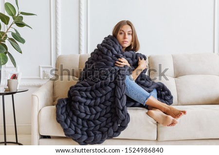Young beautiful woman in warm chunky knitted blanket at home. Model fashion shooting. Autumn, winter season.
Cozy winter style.


