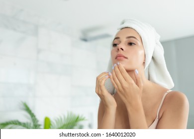 Young Beautiful Woman Wearing Bath Towel And Underwear Standing In Bathroom And Looking For Or Squeezing Acne On Chin. Mirror Reflection. Ugly Problem Teen Girl Skin, Pimples. Skincare And Beauty