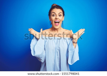 Young beautiful woman wearing bun hairstyle over blue isolated background celebrating crazy and amazed for success with arms raised and open eyes screaming excited. Winner concept