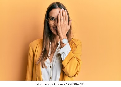 Young Beautiful Woman Wearing Business Style And Glasses Covering One Eye With Hand, Confident Smile On Face And Surprise Emotion. 