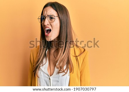 Young beautiful woman wearing business style and glasses angry and mad screaming frustrated and furious, shouting with anger. rage and aggressive concept. 