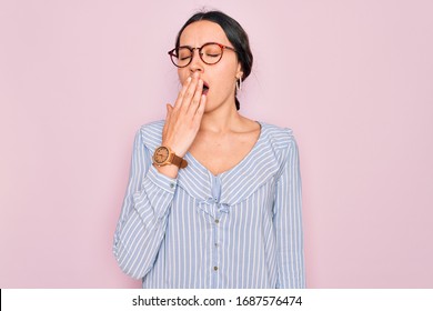 Young beautiful woman wearing casual striped shirt and glasses over pink background bored yawning tired covering mouth with hand. Restless and sleepiness.