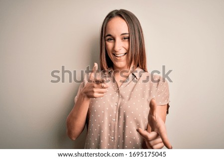 Young beautiful woman wearing casual shirt standing over isolated white background pointing fingers to camera with happy and funny face. Good energy and vibes.