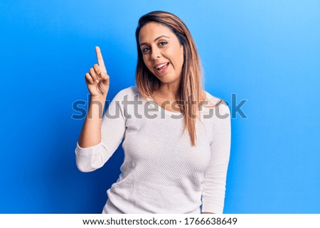 Young beautiful woman wearing casual t shirt smiling with an idea or question pointing finger up with happy face, number one 
