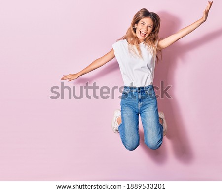 Young beautiful woman wearing casual clothes smiling happy. Jumping with smile on face and arms opened over isolated pink background