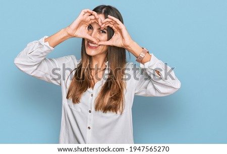 Young beautiful woman wearing casual clothes doing heart shape with hand and fingers smiling looking through sign 
