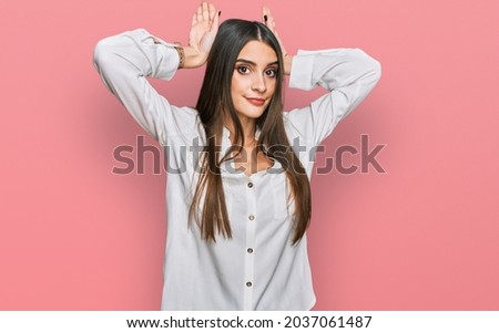 Young beautiful woman wearing casual white shirt doing bunny ears gesture with hands palms looking cynical and skeptical. easter rabbit concept. 