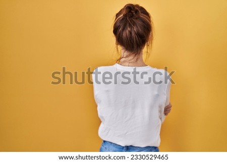 Young beautiful woman wearing casual shirt over yellow background standing backwards looking away with crossed arms 