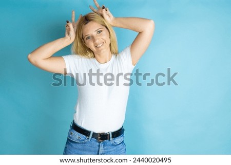 Young beautiful woman wearing casual t-shirt over isolated blue background Posing funny and crazy with fingers on head as bunny ears, smiling cheerful