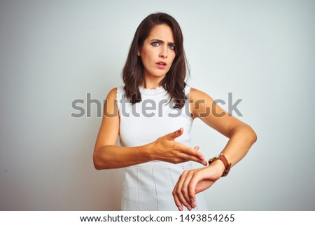 Young beautiful woman wearing dress standing over white isolated background In hurry pointing to watch time, impatience, upset and angry for deadline delay