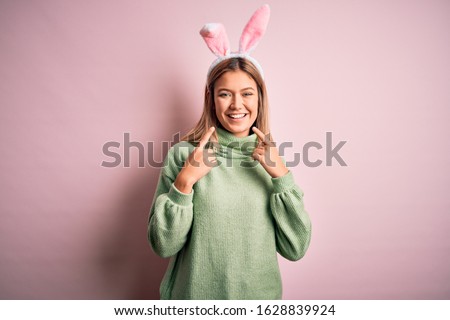 Young beautiful woman wearing easter rabbit ears standing over isolated pink background smiling cheerful showing and pointing with fingers teeth and mouth. Dental health concept.