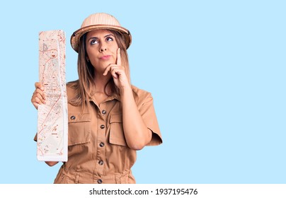 Young Beautiful Woman Wearing Explorer Hat Holding Map Serious Face Thinking About Question With Hand On Chin, Thoughtful About Confusing Idea 