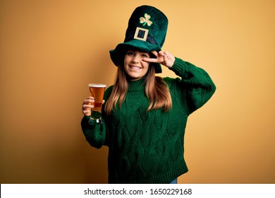 Young beautiful woman wearing green hat drinking glass of beer on saint patricks day Doing peace symbol with fingers over face, smiling cheerful showing victory