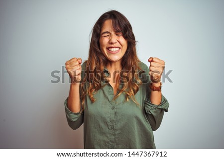 Young beautiful woman wearing green shirt standing over grey isolated background excited for success with arms raised and eyes closed celebrating victory smiling. Winner concept.