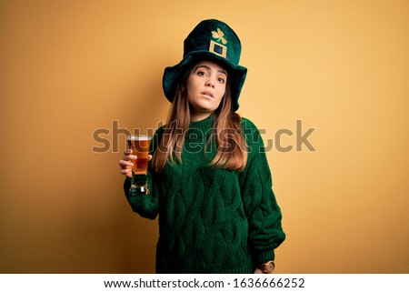Young beautiful woman wearing green hat drinking glass of beer on saint patricks day looking sleepy and tired, exhausted for fatigue and hangover, lazy eyes in the morning.
